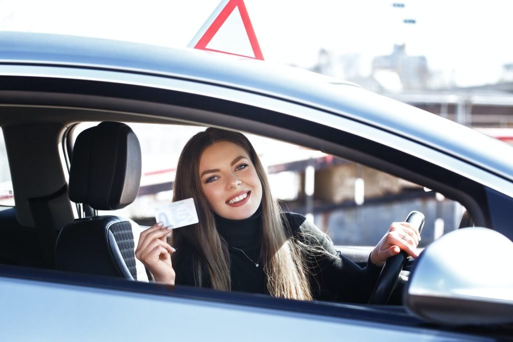 Joyful girl driving a training car with a drivers license card in her hands